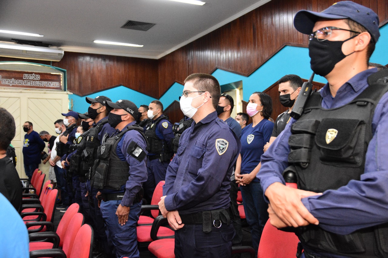 Servidores da Segurança Pública Municipal enfileirados em pé, um ao lado do outro, no auditório da Estação das Artes Elizeu Ventania. Eles usam máscara, uniforme azul com colete, alguns utilizam boné e óculos de grau.